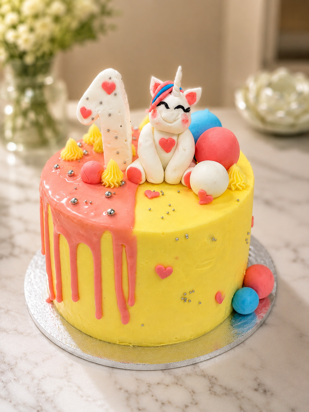 Eggless yellow and pink unicorn first birthday drip cake with fondant unicorn topper, number one and coloured spheres, handcrafted in Bendigo by Cakery Corner